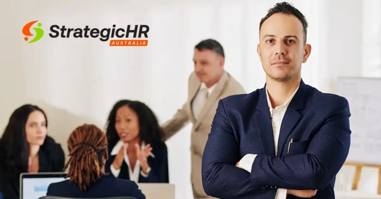 A man in a suit stands with arms crossed in the foreground, while three people have a discussion at a table in the background. The StrategicHR Australia logo is displayed in the top left corner.