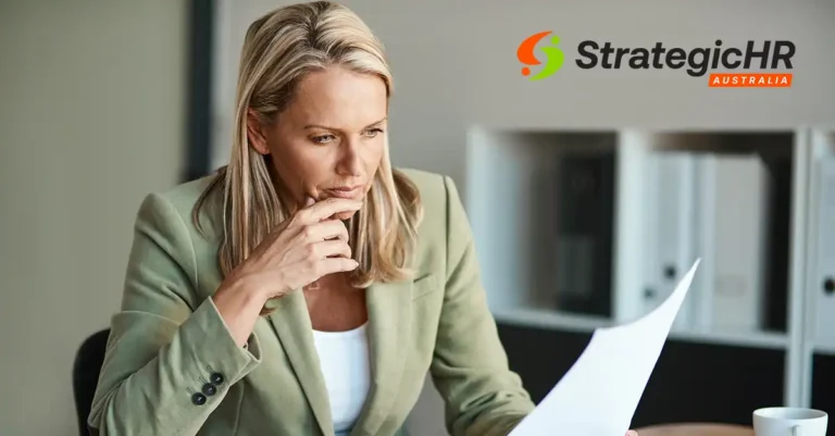 A woman in a green blazer sits at a desk, holding and reading a document with a thoughtful expression, staying informed on workplace law updates. The Strategic HR Australia logo appears in the top right corner.