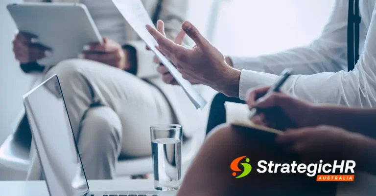 Three people sit in a business meeting. One holds papers, another writes in a notebook, fostering clarity of expectations. A laptop and glass of water are on the table, with the StrategicHR Australia logo visible in the lower right corner.