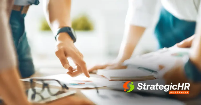 Three people stand around a table, reviewing and pointing at printed charts and documents. The logo “Strategic HR Australia” appears in the bottom right corner.