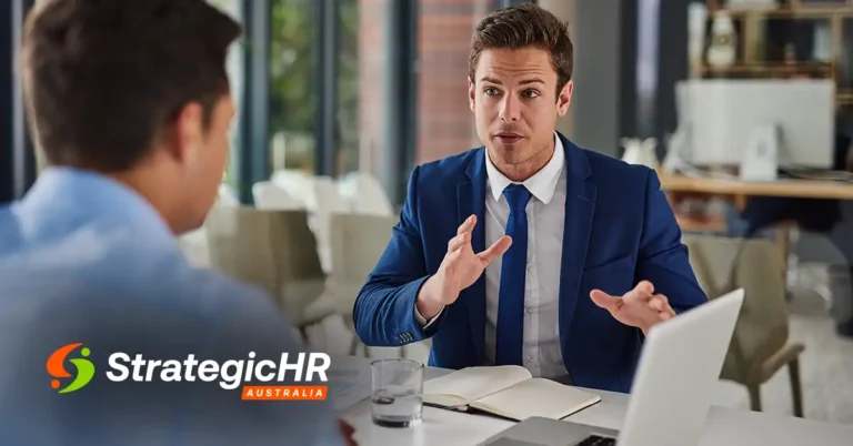 Two men in business attire discuss solutions at a desk with a laptop, notebook, and glass of water. The logo "Strategic HR Australia" highlights their expertise in fractional HR Australia services.